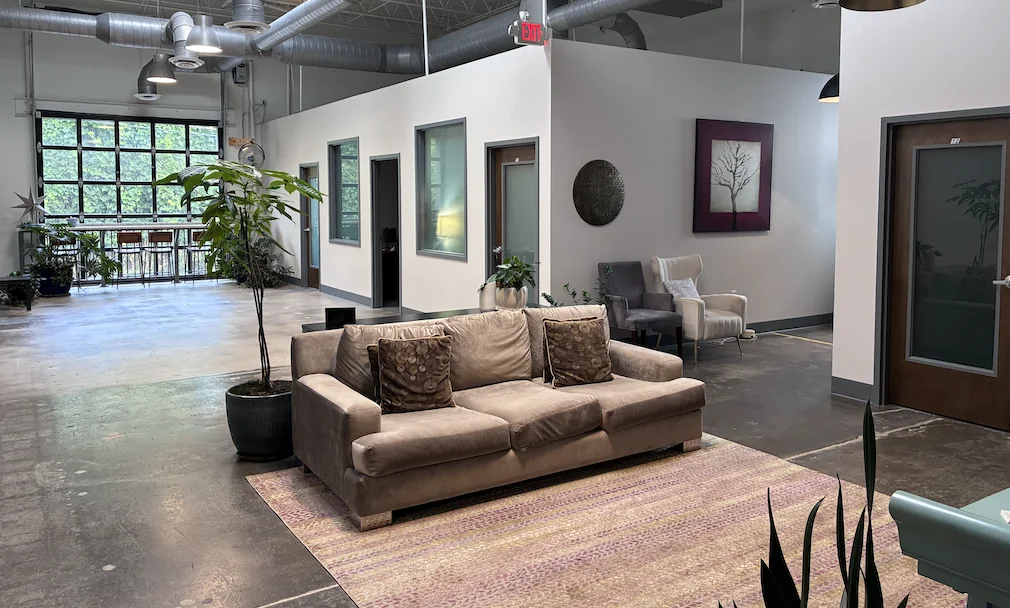 Espaço interno compartilhado da Midtown Psychotherapy Associates com sofá, poltronas, plantas e janelas amplas.